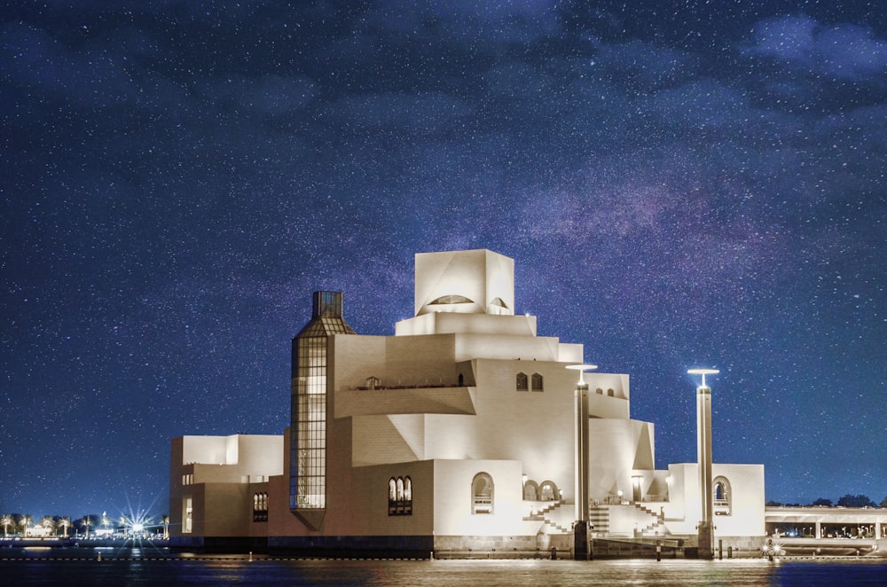 white concrete building in front of calm body of water under galaxy