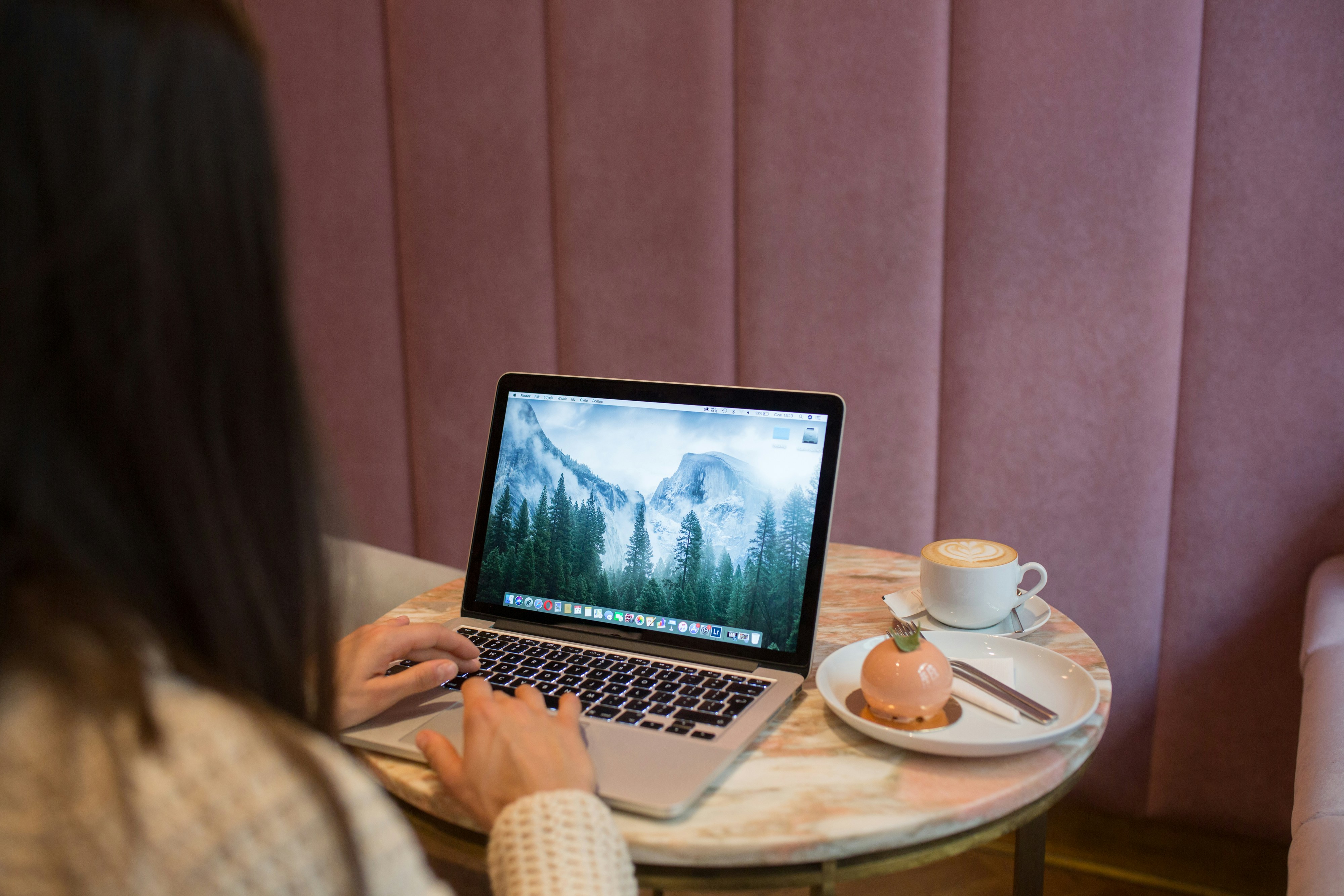 Female hands typing on MacBook pro in a pink cafe. Lunchtime break.
