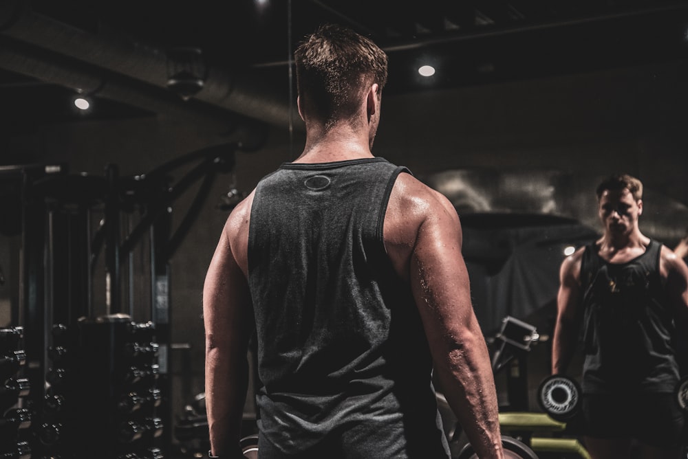 man in gray tank top doing exercise holding weight inside gym