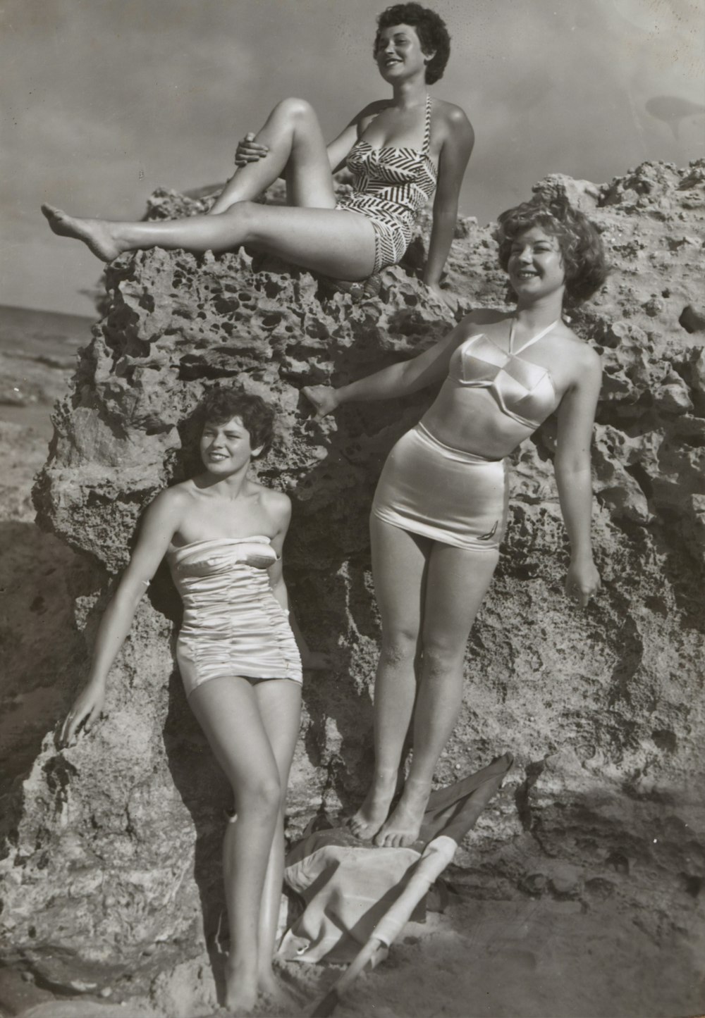 Foto en escala de grises de tres mujeres de pie y sentadas en las rocas