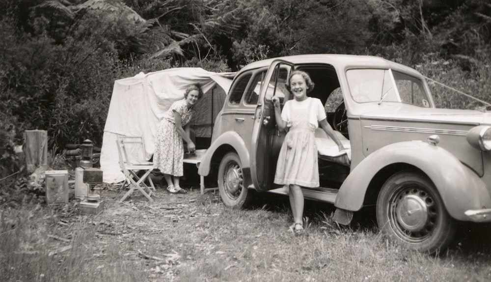 grayscale photo of girl beside car