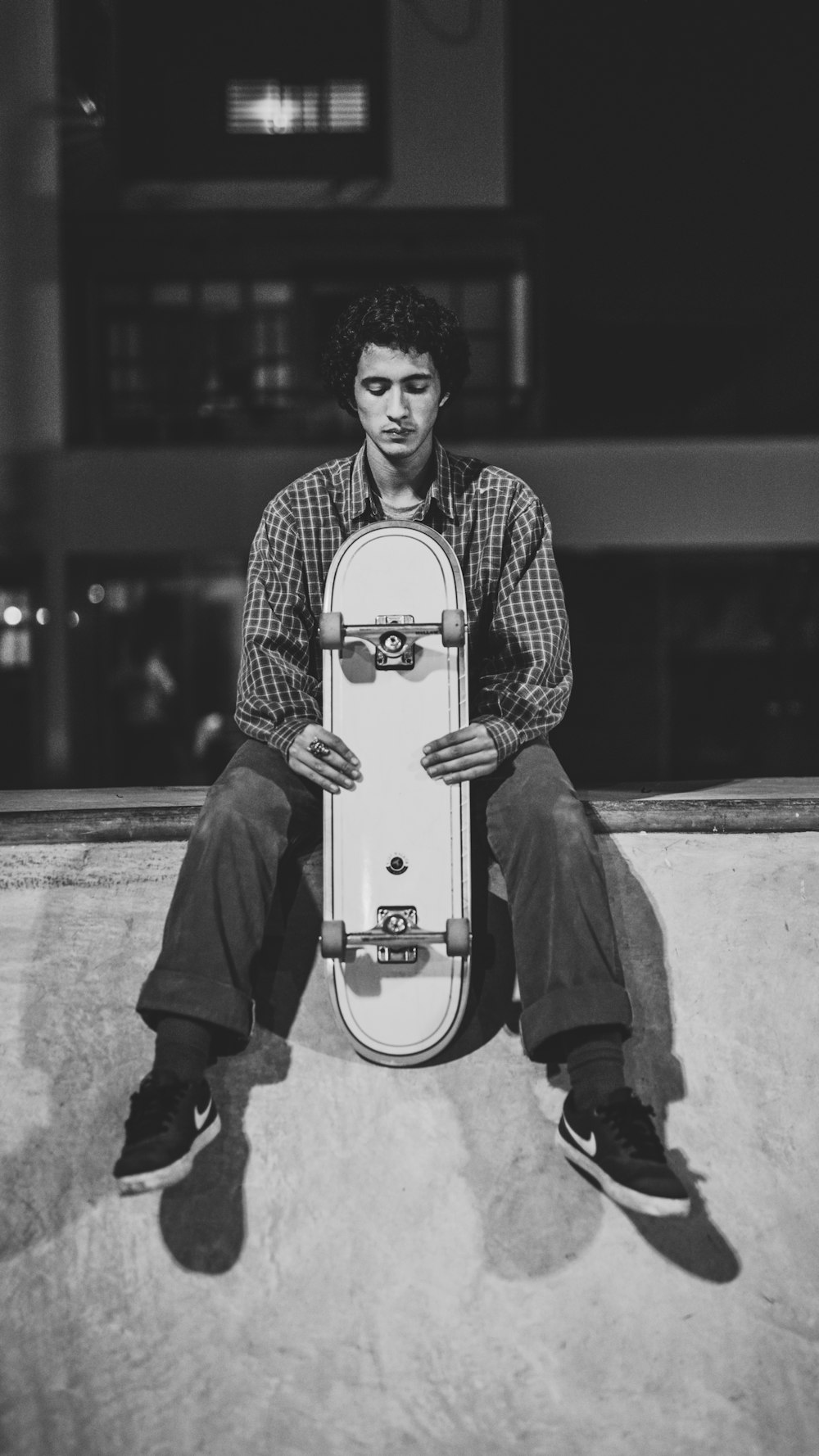 grayscale photography of man holding skateboard while sitting