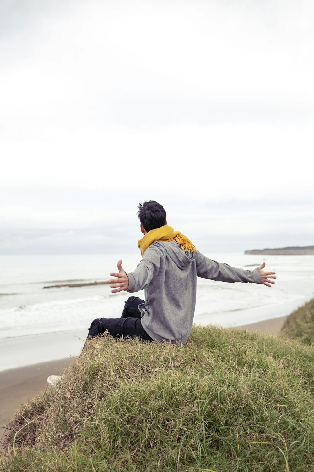 man open wide arms while sitting on grass