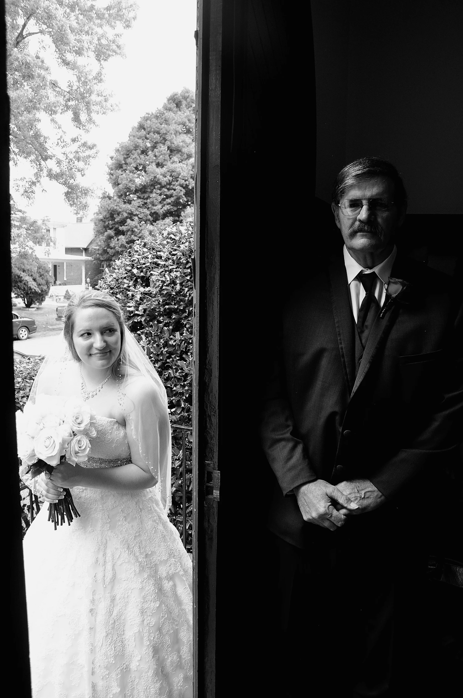 A bride waiting in daylight beside a man standing in a dark doorway