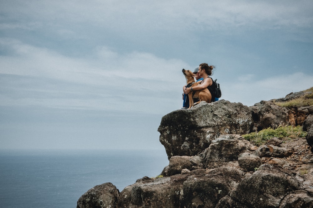 woman sitting beside dog on cliff during daytime