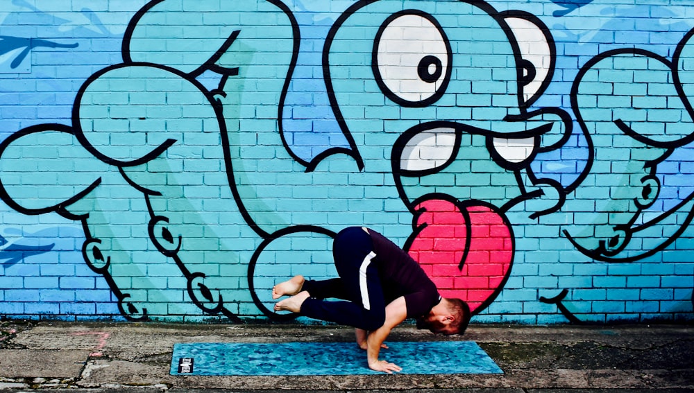 man wearing black t-shirt doing stunt near graffiti wall