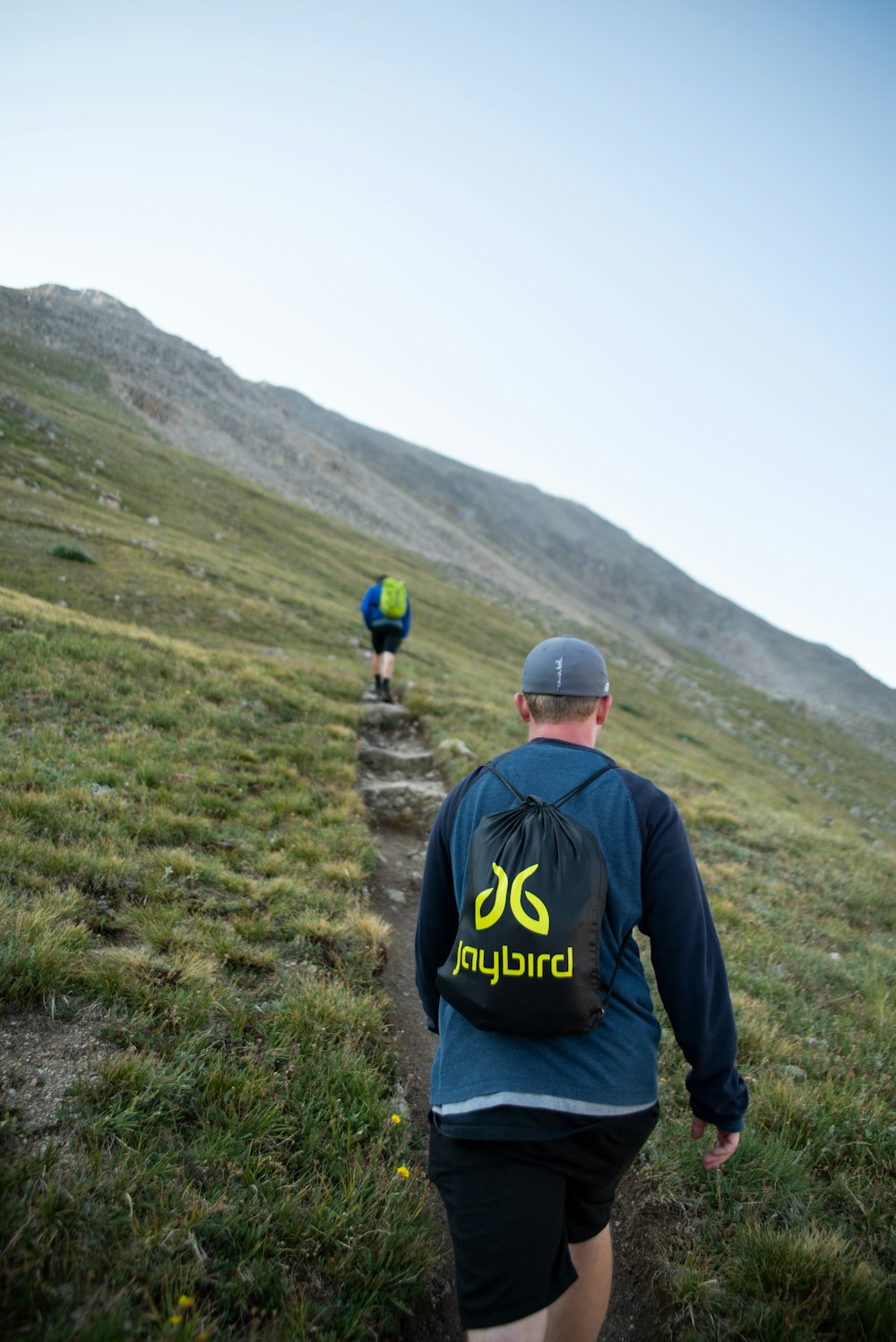 Zwei Männer wandern tagsüber in der Nähe von Green Field unter weißem und blauem Himmel