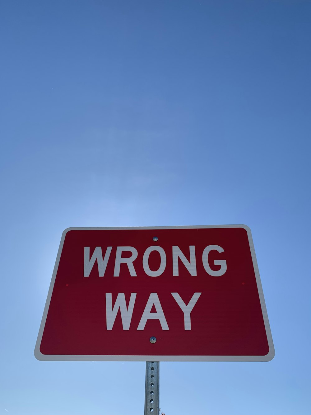 a red wrong way sign with a sky background