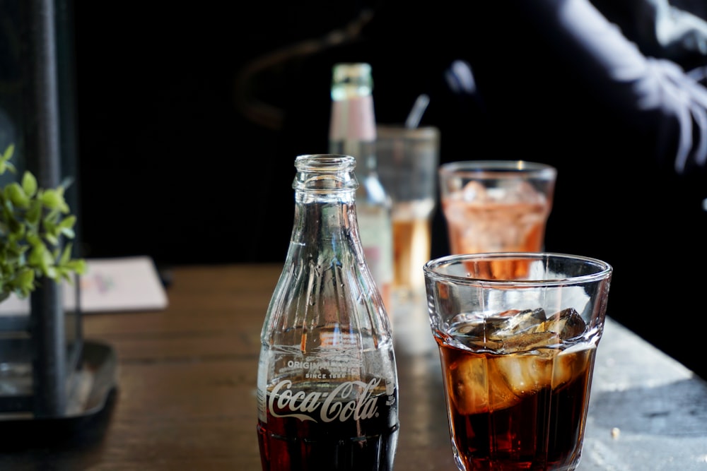 Coca-Cola glass bottle beside a glass of soda with ice cubes