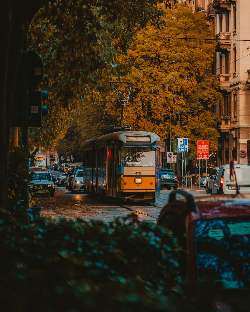 gray and orange tram between trees and buildings