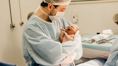 man in lab suit and mask carrying newborn baby