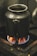 A metal container is placed on a gas stove with a visible blue and orange flame underneath, indicating it is being heated. The surrounding area suggests an industrial or heavily used kitchen setting.