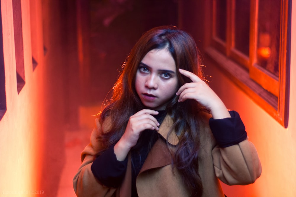 woman wearing brown coat standing while touching her hair