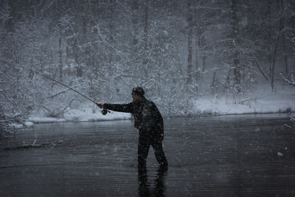 grayscale photography of man fishing in body of water while snowing