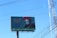 A large billboard advertising a 'Festival de Día de Muertos' features an image of a person with a traditional Day of the Dead face paint and wearing vibrant red marigold flowers in their hair. The background is teal with decorative patterns and Spanish text. Visible power lines and a clear blue sky can be seen.
