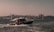 A boat is traveling through the water with seagulls flying overhead. In the background, a cityscape features several mosques with domes and minarets, under a clear sky.
