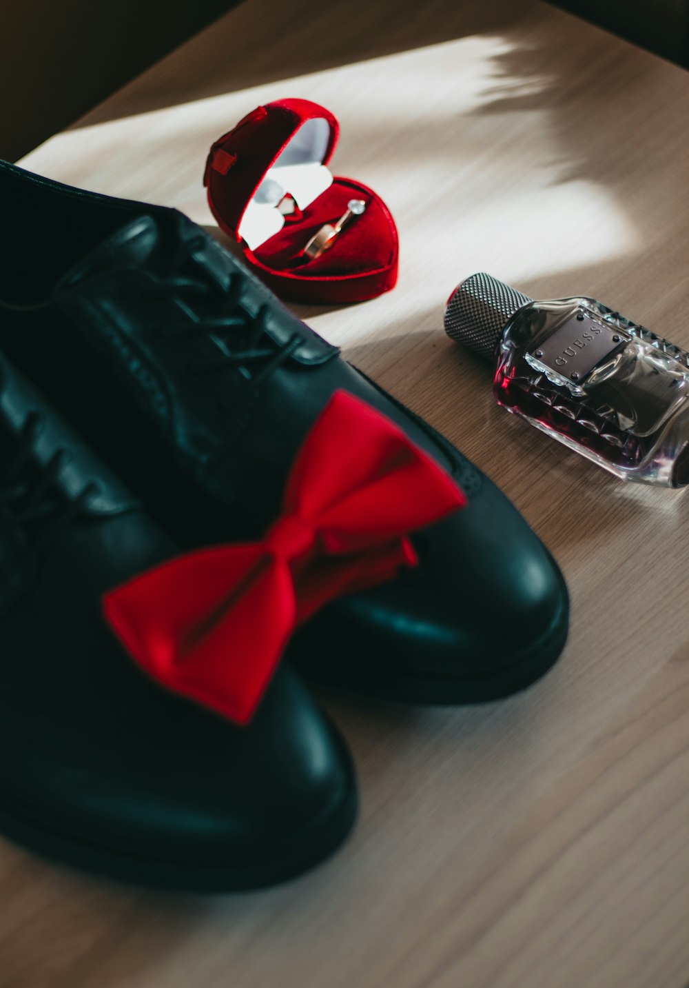 pair of black leather dress shoes beside wedding ring and perfume bottle
