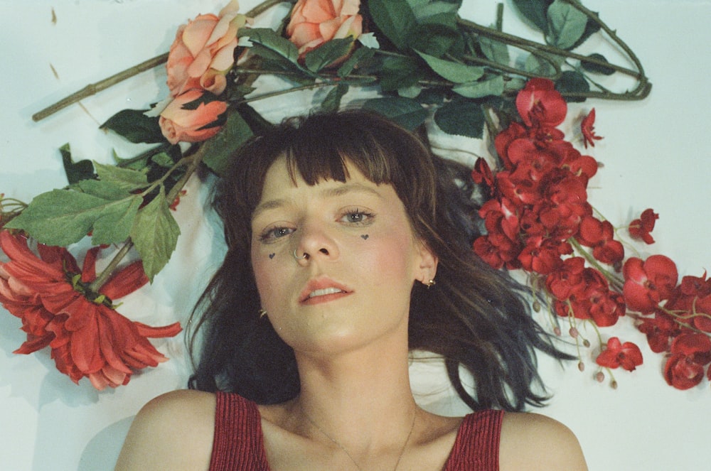 woman lying on bed beside red petaled flowers