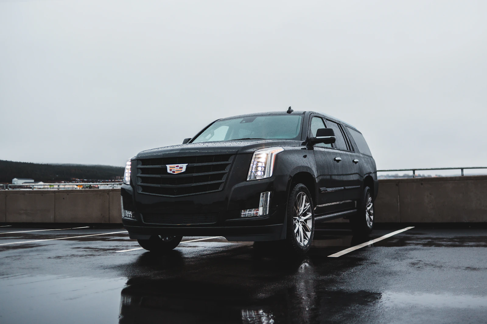 Black Cadillac Escalade ESV on a rain-washed parking deck