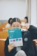 Smiling young student holding a workbook during an online language lesson.