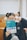 A person is holding a book titled 'College English Creative Communication' in front of their face, while making a peace sign gesture with their hand. The setting appears to be a classroom with wooden desks and several people in the background, slightly blurred.