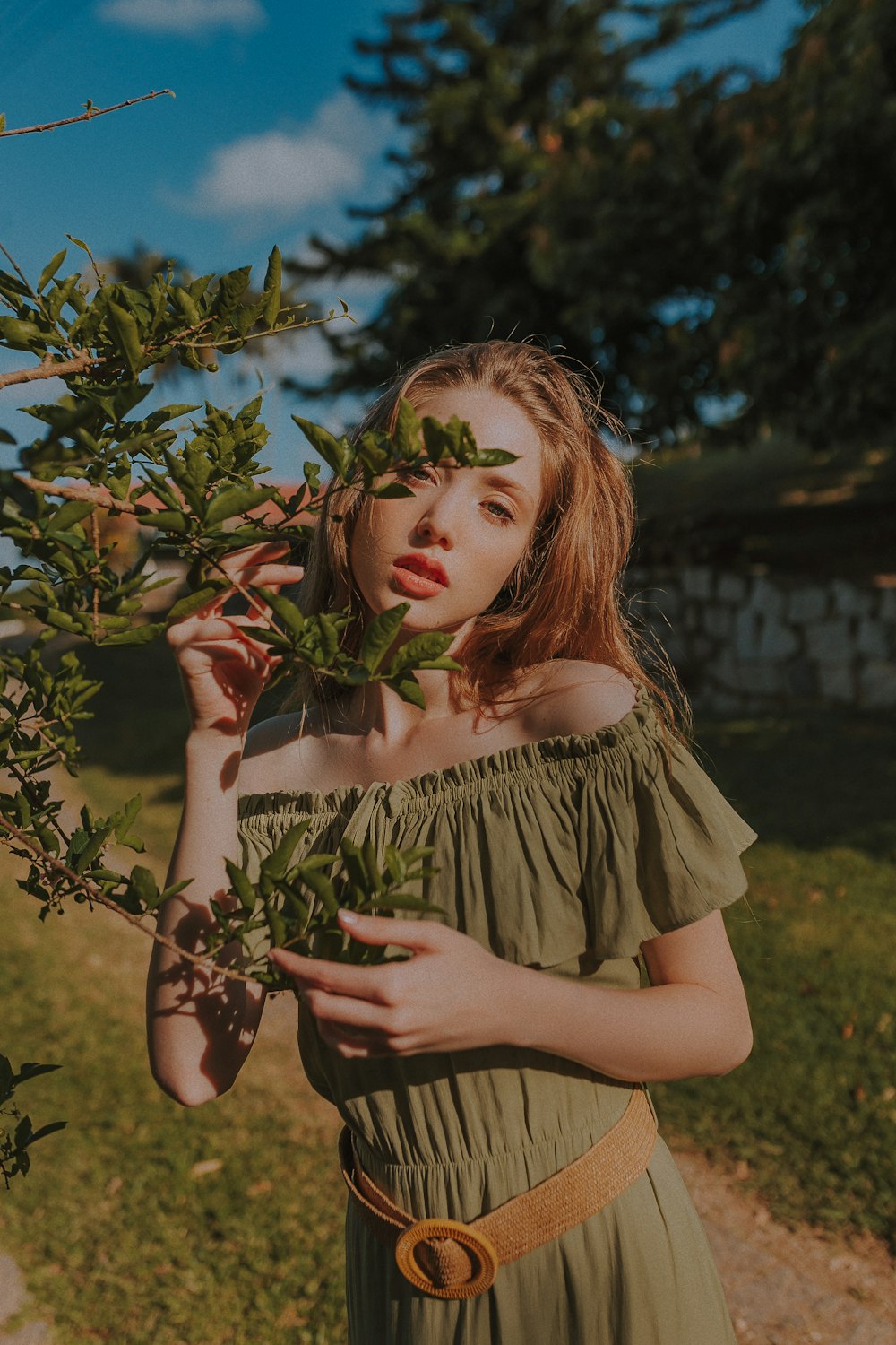woman in green off-shoulder dress standing beside green leafed plant