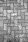An arrangement of interlocking concrete pavement blocks, featuring a repetitive zigzag pattern. The surface of the blocks shows signs of wear and has varying shades of gray, with some visible dirt and small patches of discoloration.