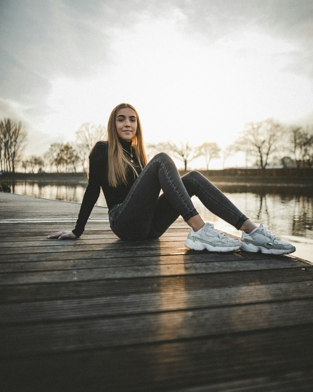 woman sitting on brown wooden dock bridge near body of water