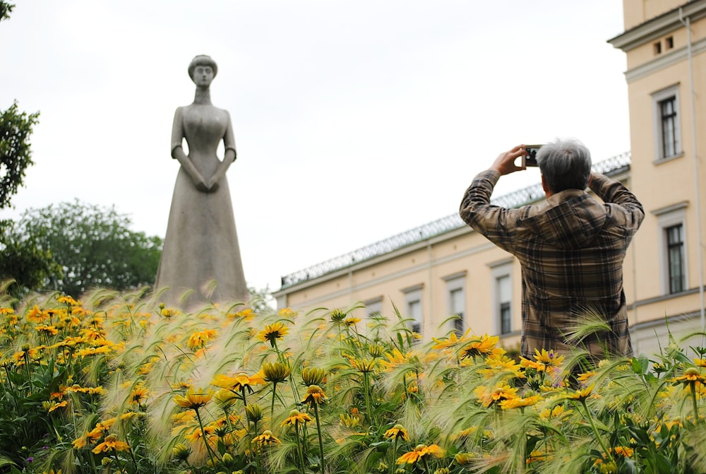 man standing while taking picture of woman statue