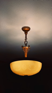 An ornate ceiling light fixture with a round, warm-hued glass shade hanging from a decorative bronze or brass holder. The shade features intricate designs, adding an elegant touch to the room's interior.