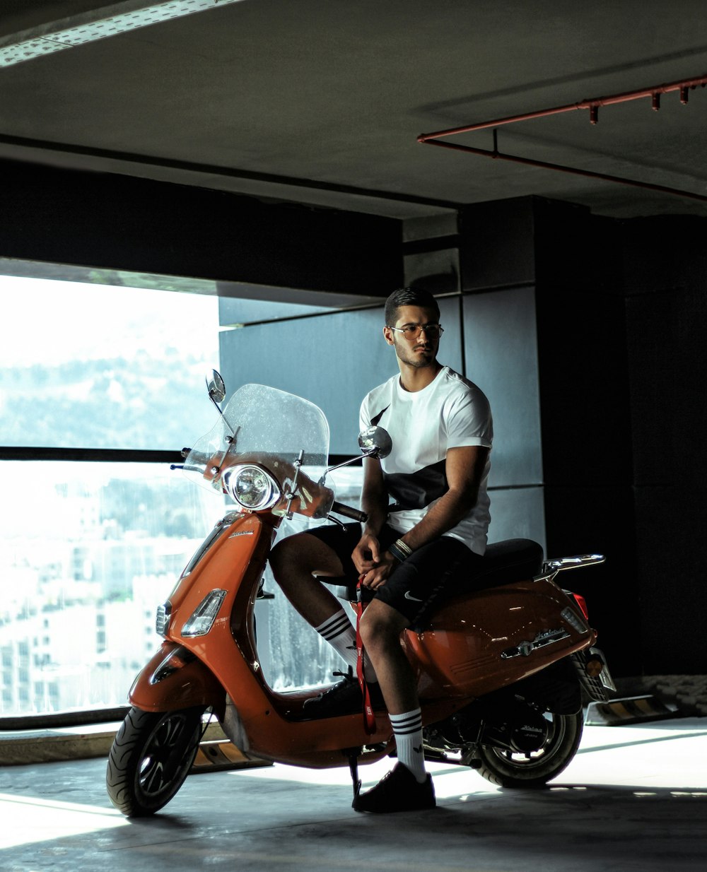 man wearing white crew-neck t-shirt sitting on orange motor scooter