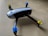 Quadcopter drone with black and white body and propellers featuring blue and yellow tops placed on a light wooden surface.