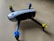 Quadcopter drone with black and white body and propellers featuring blue and yellow tops placed on a light wooden surface.