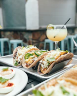 three tacos on plate beside margarita