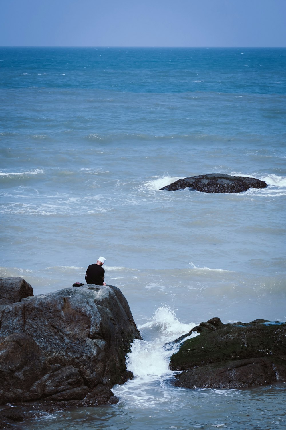 man sitting on rock on sea during daytime