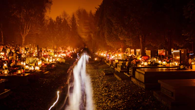 Golden and burgundy cemetery candles glowing softly on a stone grave at dusk.