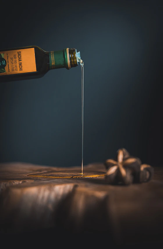 Fio fino de óleo dourado sendo despejado sobre madeira, luz quente