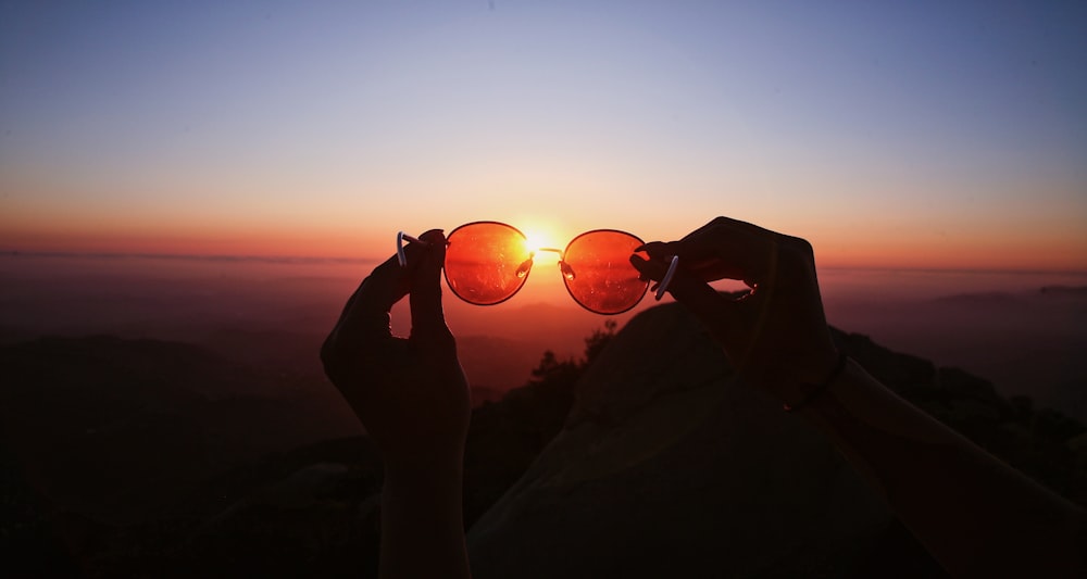 low-light photo of person holding sunglasses against the sun
