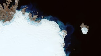 A satellite image shows a large expanse of icy terrain, characterized by predominantly white and brown patches along the edges, with dark blue and black waters surrounding it. An isolated, rounded icy landmass appears in the water to the right, slightly separated from the main ice field.