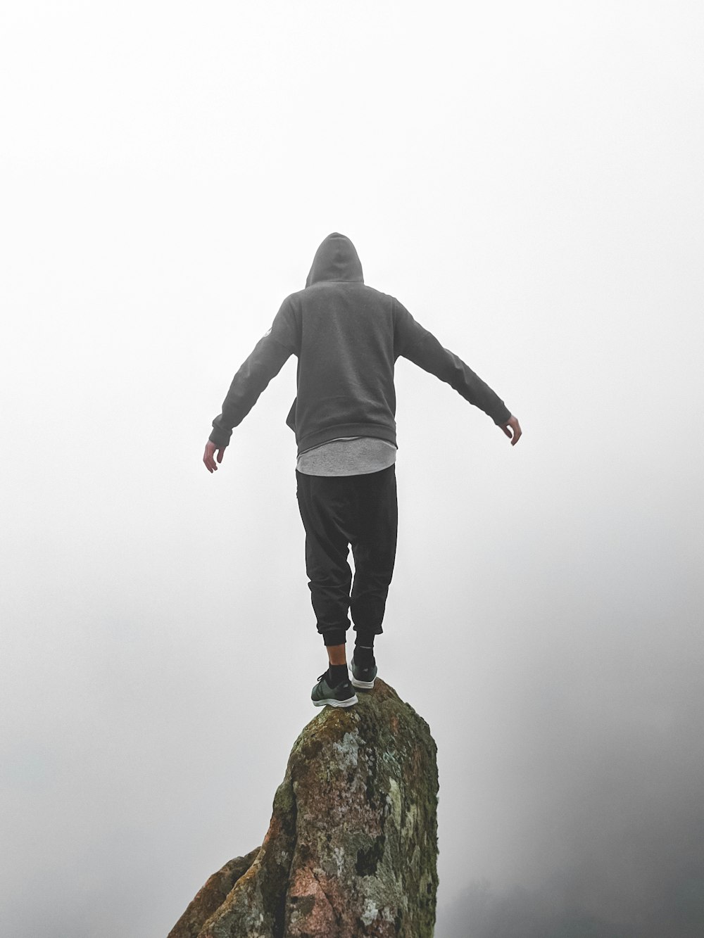 Person im grauen Kapuzenpullover steht auf Felsen