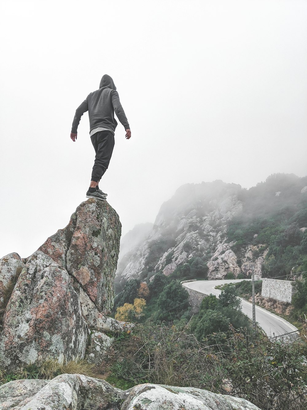 Mann in grauem Pullover und grauer Trainingshose steht auf Felsen