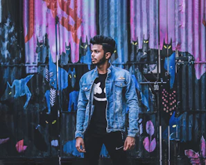 Model wearing a grimquirk jacket with a slightly unimpressed creature patch, standing against a graffiti wall