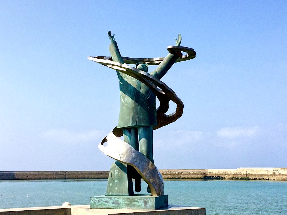 round grey metal statue beside body of water during daytime