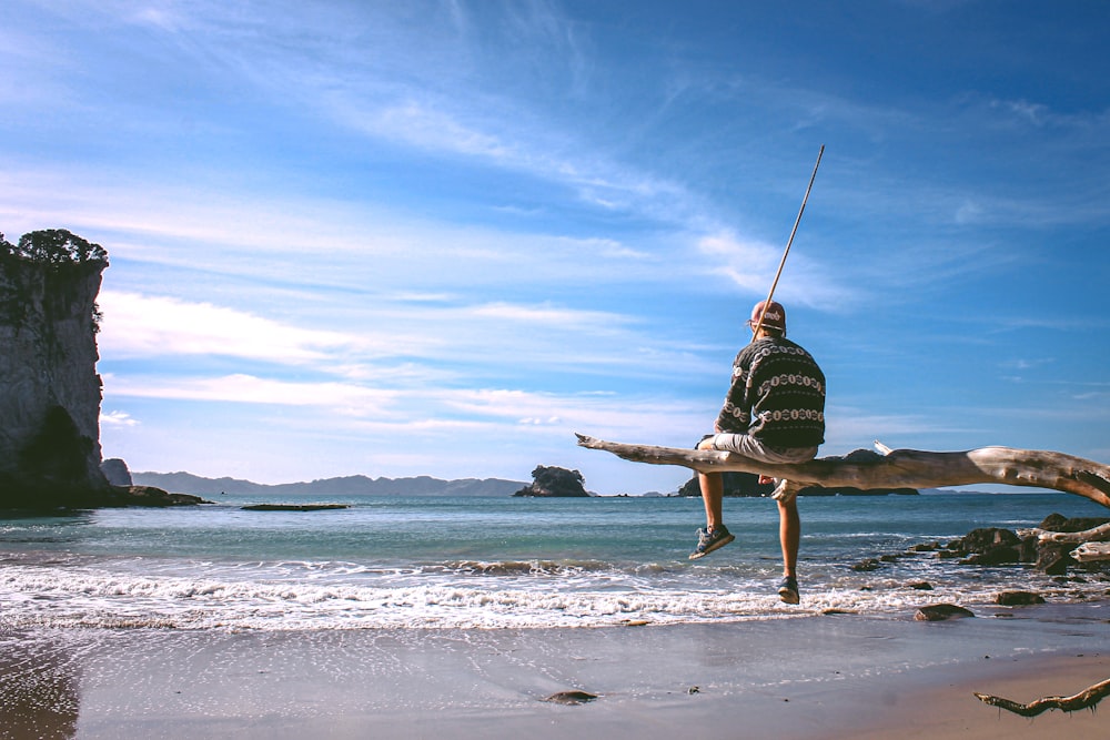 person sitting on driftwood near seashore during daytime