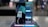 A smartphone is displayed on a stand, showcasing its sleek design. Behind it, a reflective surface enhances its modern look. The device's screen features a stylized graphic, and a stylus is placed to the side.
