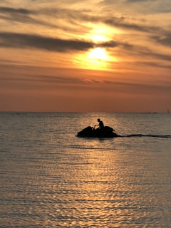 Sunset casting golden light over calm waters with a lone jet ski gliding smoothly.