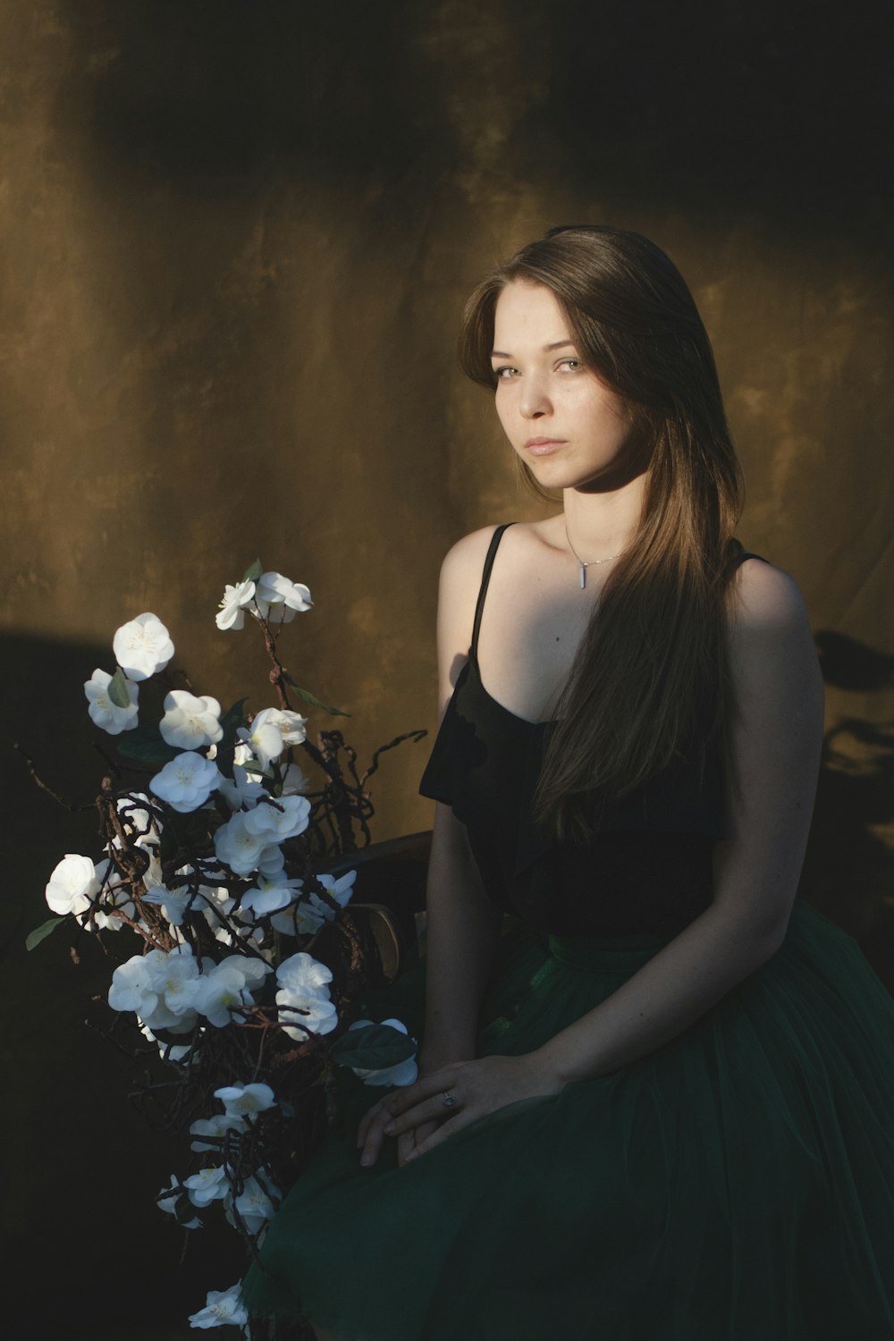 low-light photo of woman sitting on chair beside white flower