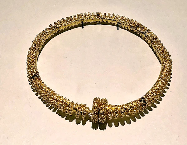 Close-up of a luxurious golden necklace with laurel crown details on a vibrant background.