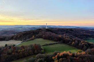 A panoramic view of rolling hills dotted with eco-friendly homes and wind turbines at sunset.