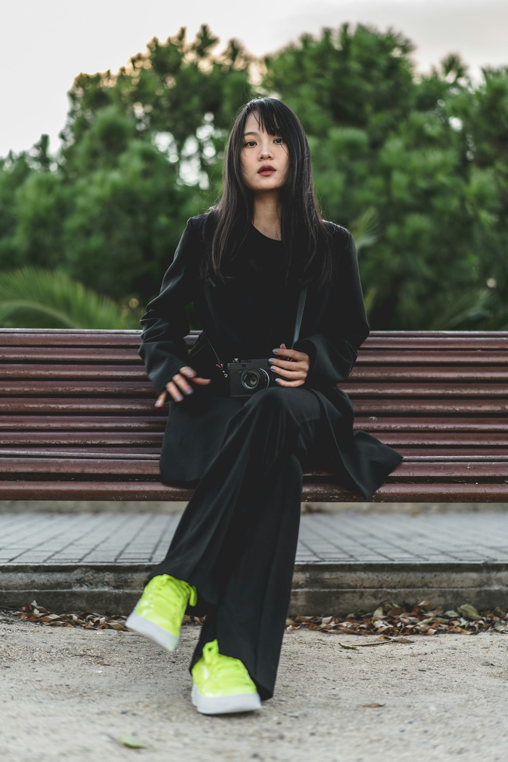 woman wearing black pea coat and black pants sitting on brown bench